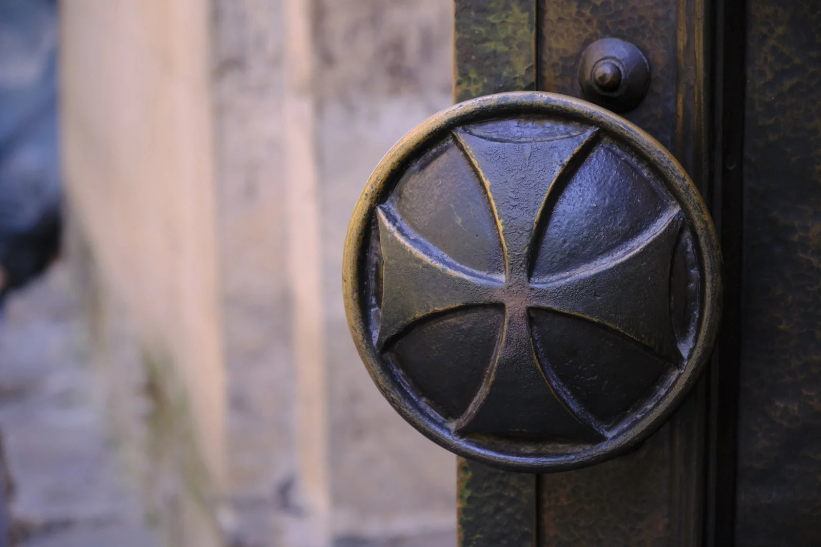 Close-up of a round metal door boss shaped like a Georgian cross on a dark door.