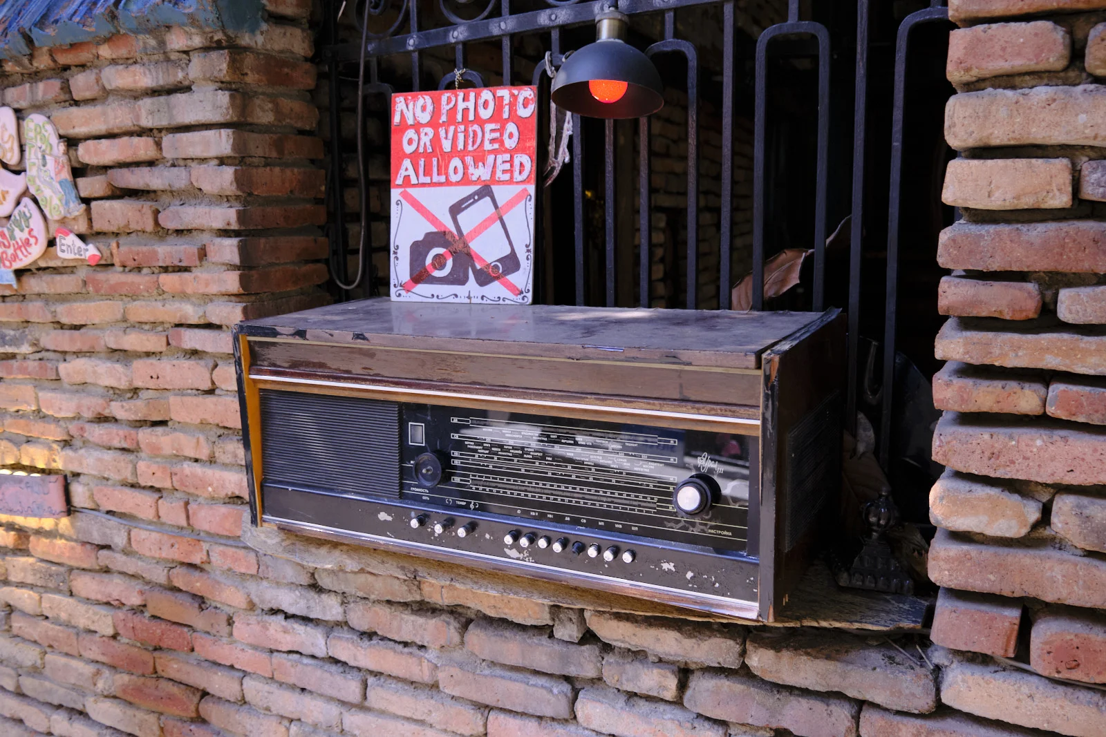 A worn wooden radio rests on a brick ledge under a sign that forbids photos and video.