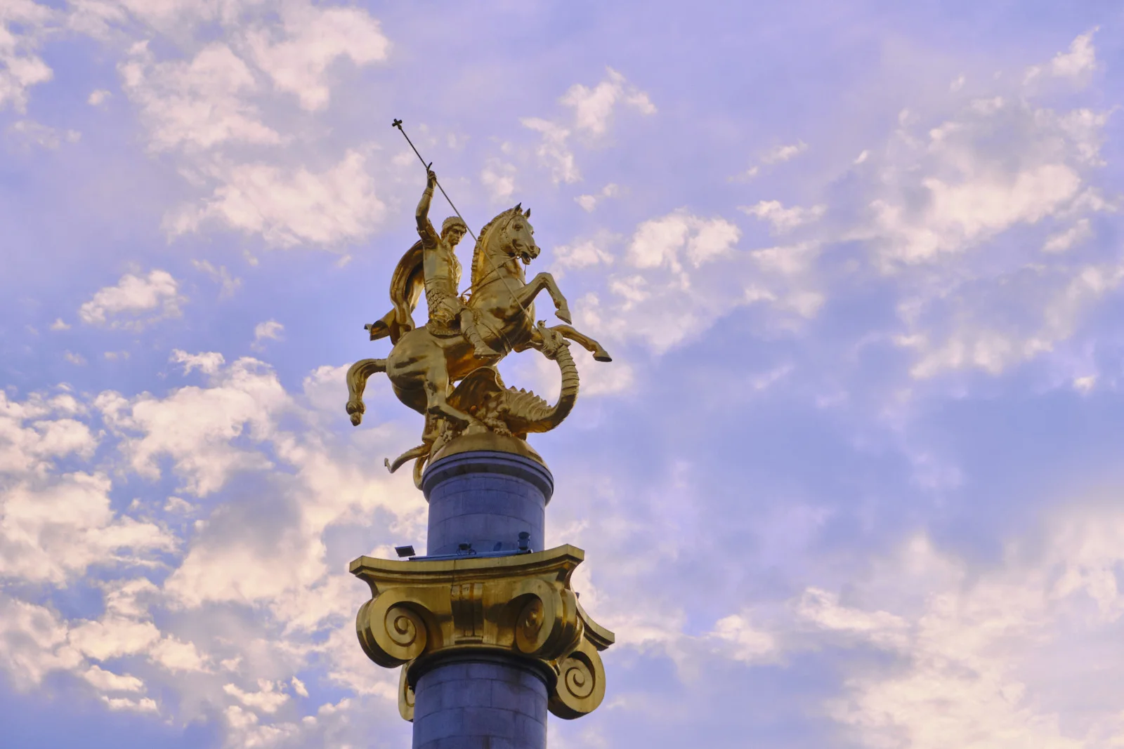 A gilded statue of St. George on a rearing horse stands atop a column against a cloudy sky.