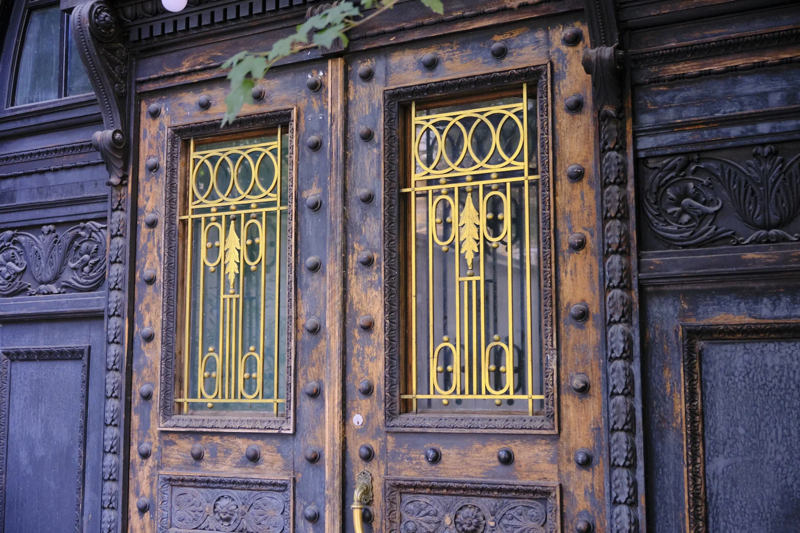 Dark wooden double doors with bright gold iron grilles and rows of metal studs.