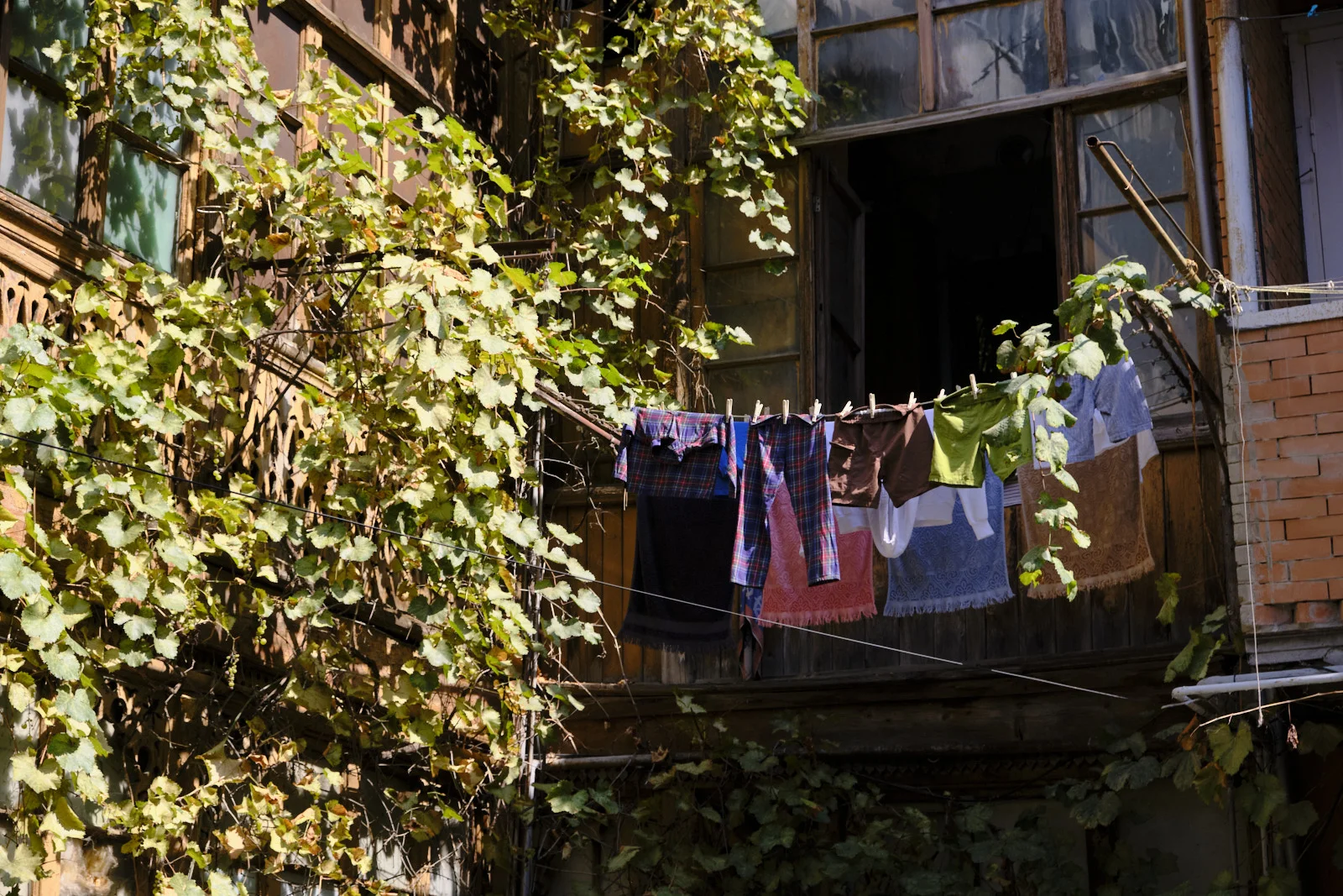 Clothes hang on a line across a vine-covered wooden balcony with an open window.