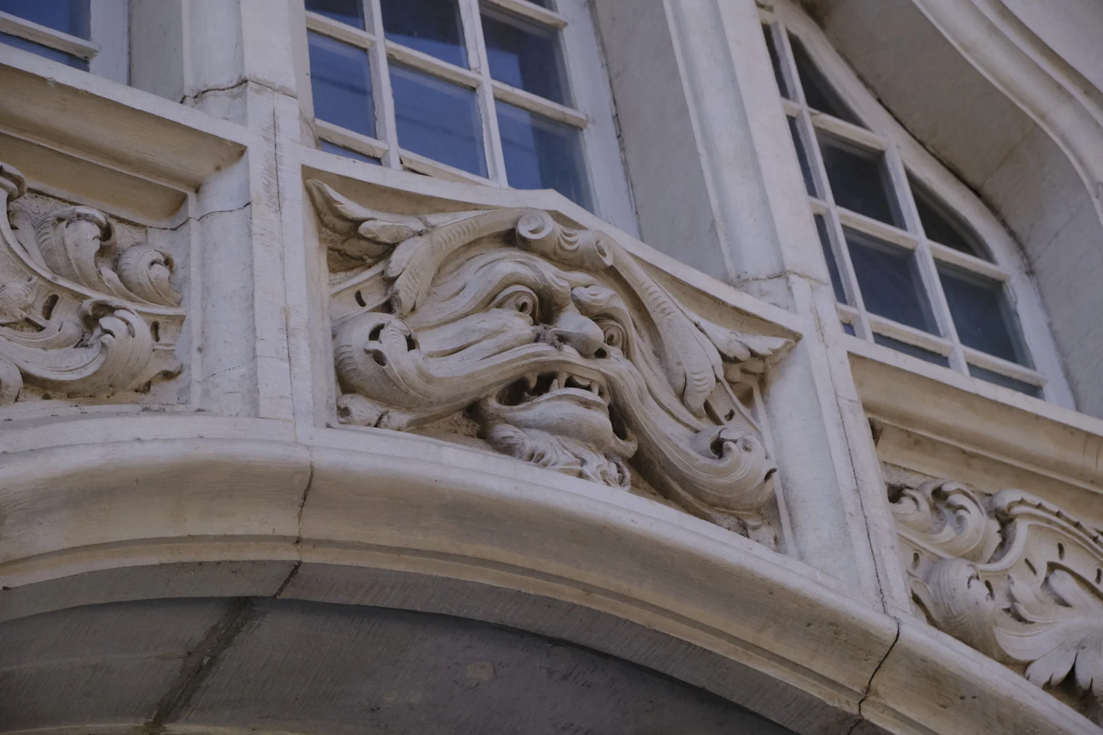 A grotesque carved face with a flowing beard under a row of windows.