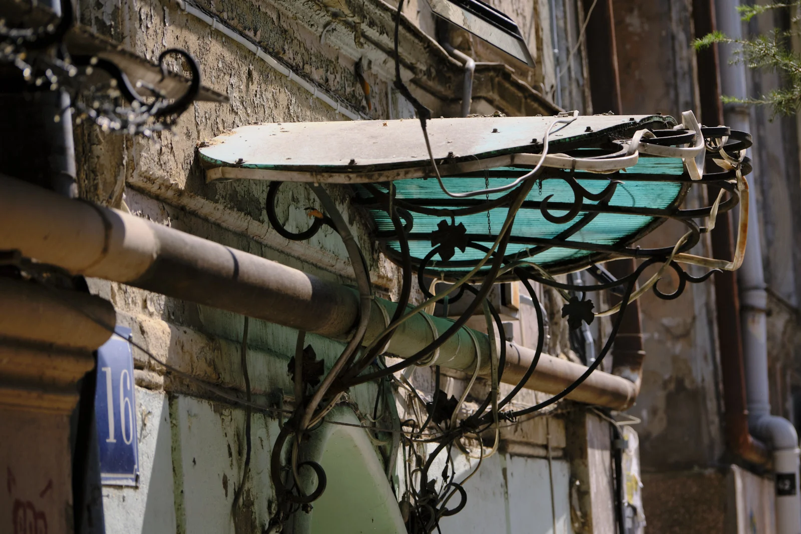 A bent iron canopy with a green panel over a doorway, beside a blue number 16 plaque.