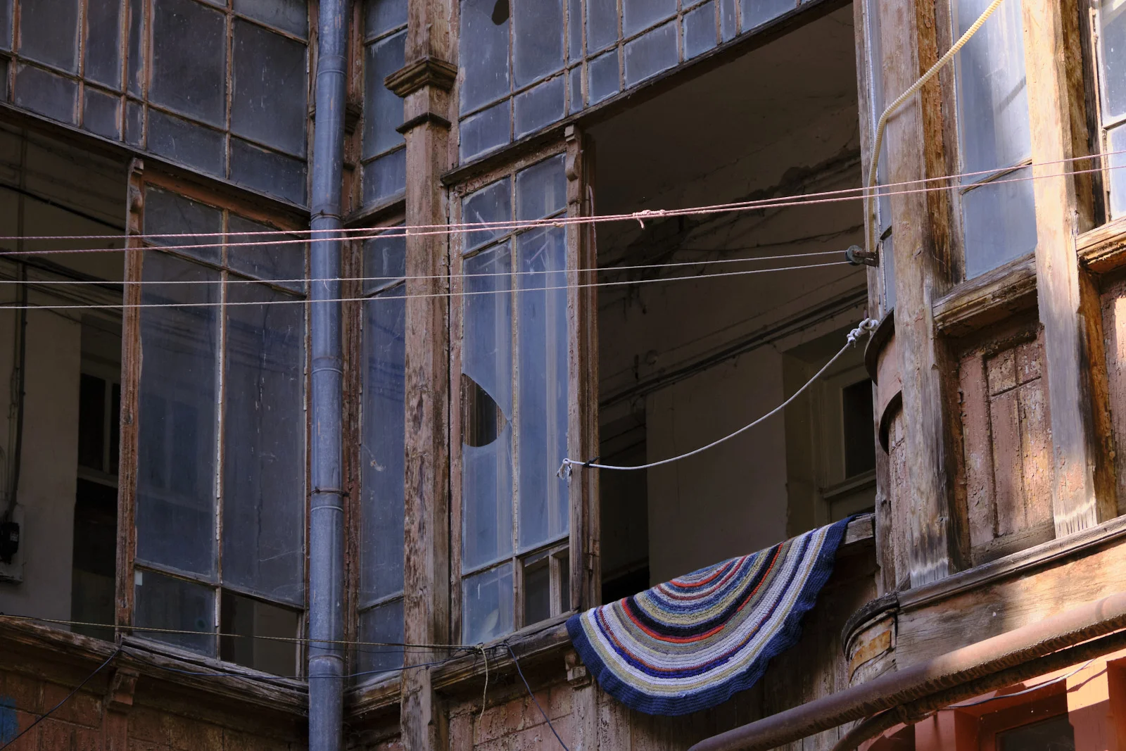 A wooden balcony of broken glass panes, with a striped semicircular rug hanging from a line.
