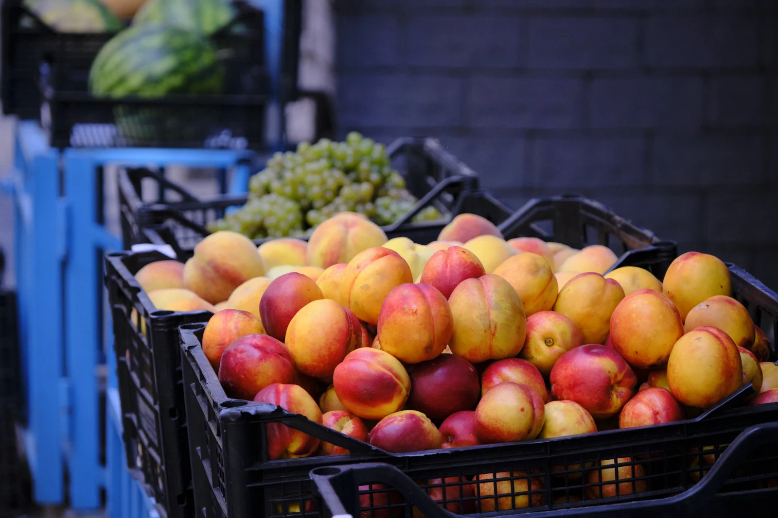Black crates piled with ripe peaches, grapes and a watermelon behind them.