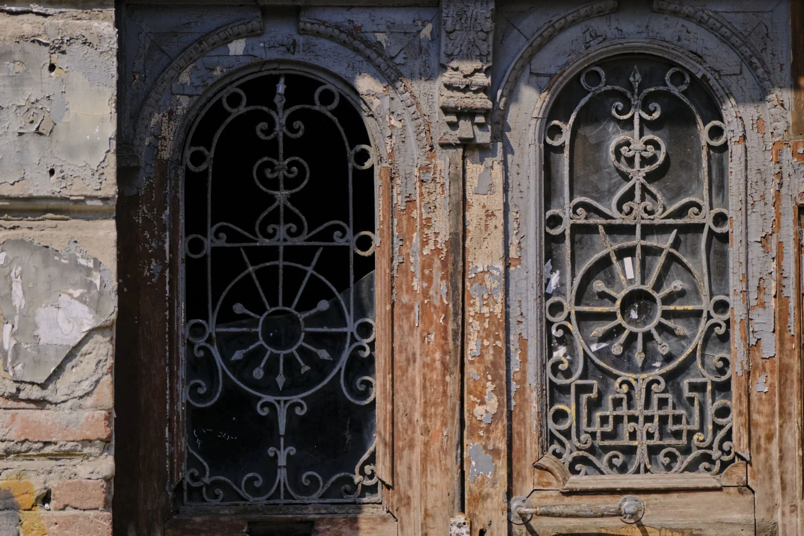 Two arched doorways in a ruined wooden frame, one grille a sunburst and the other a wheel.