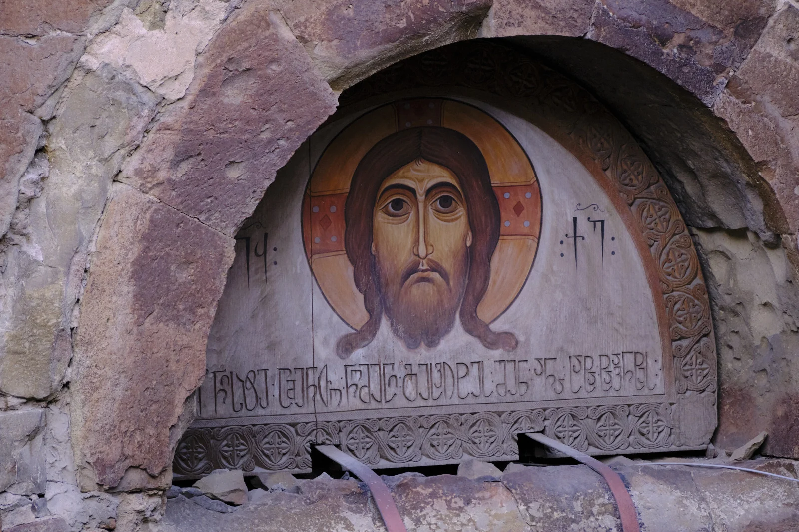 A painted icon of Christ set in a rough stone arch, with Georgian letters on either side.