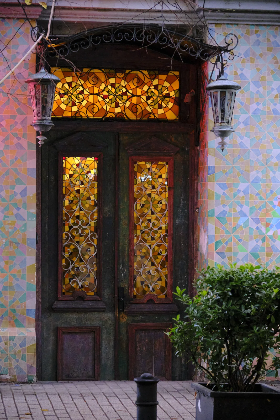 A wooden door with glowing yellow stained glass, set in a wall of pastel geometric tiles.