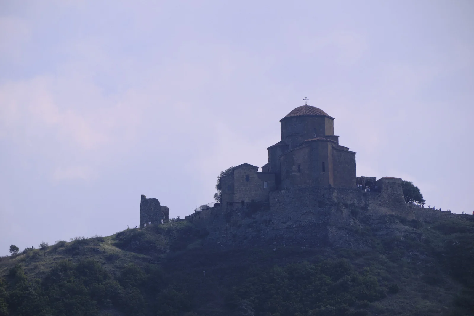 Jvari Monastery small on its rocky ridge, seen through the haze from below.
