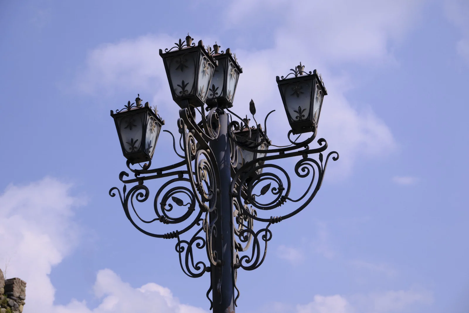 Close view of an iron lamp post with four glass lanterns against a blue sky.