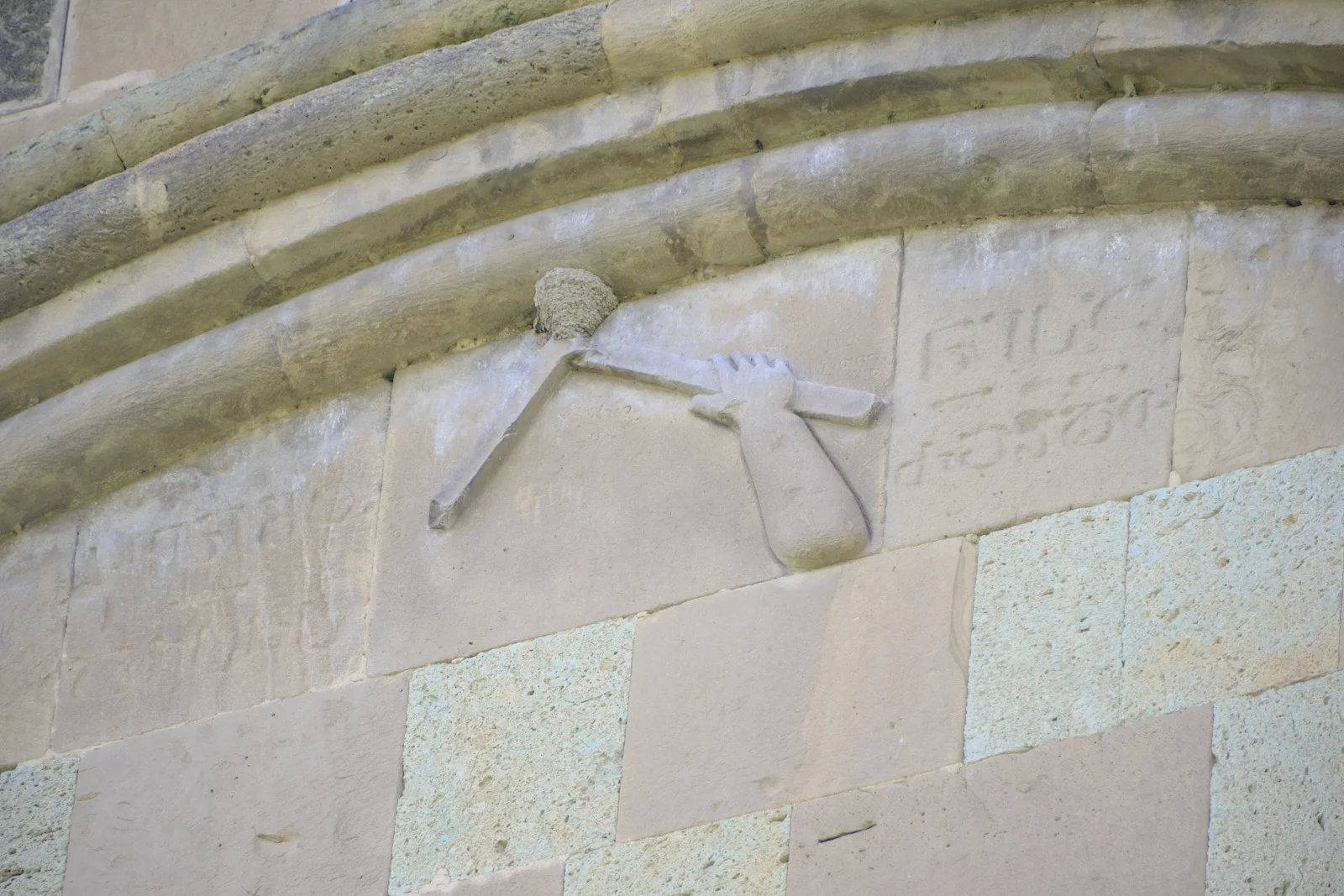 A stone relief of a hand gripping a cross, set into a pale church wall.