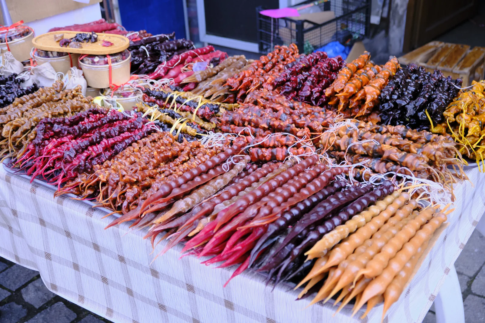 Rows of churchkhela in red, brown, and orange laid across a market table.