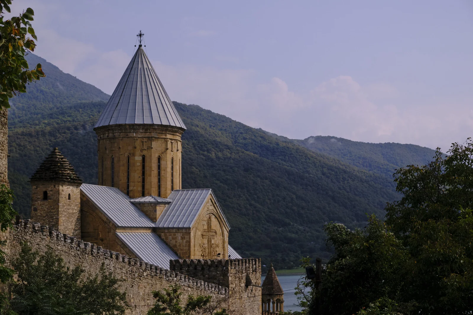 The church at Ananuri in shadow, a conical roof against forested mountains and a glimpse of the reservoir.