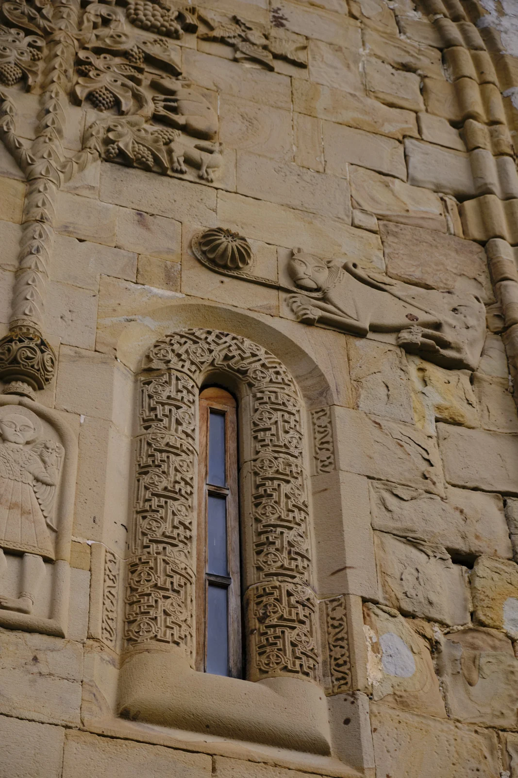 Carved stone around a narrow window: a lion, grapevines, and a standing figure.