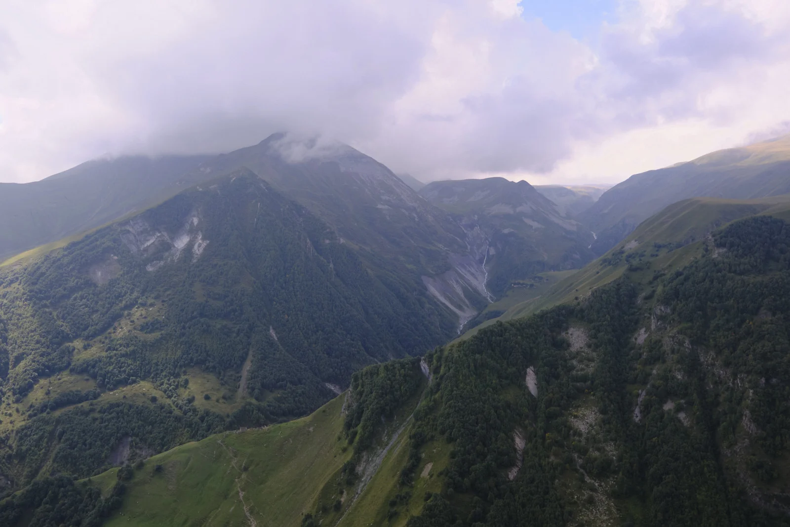 A deep green mountain valley, cloud sitting on the far ridge.
