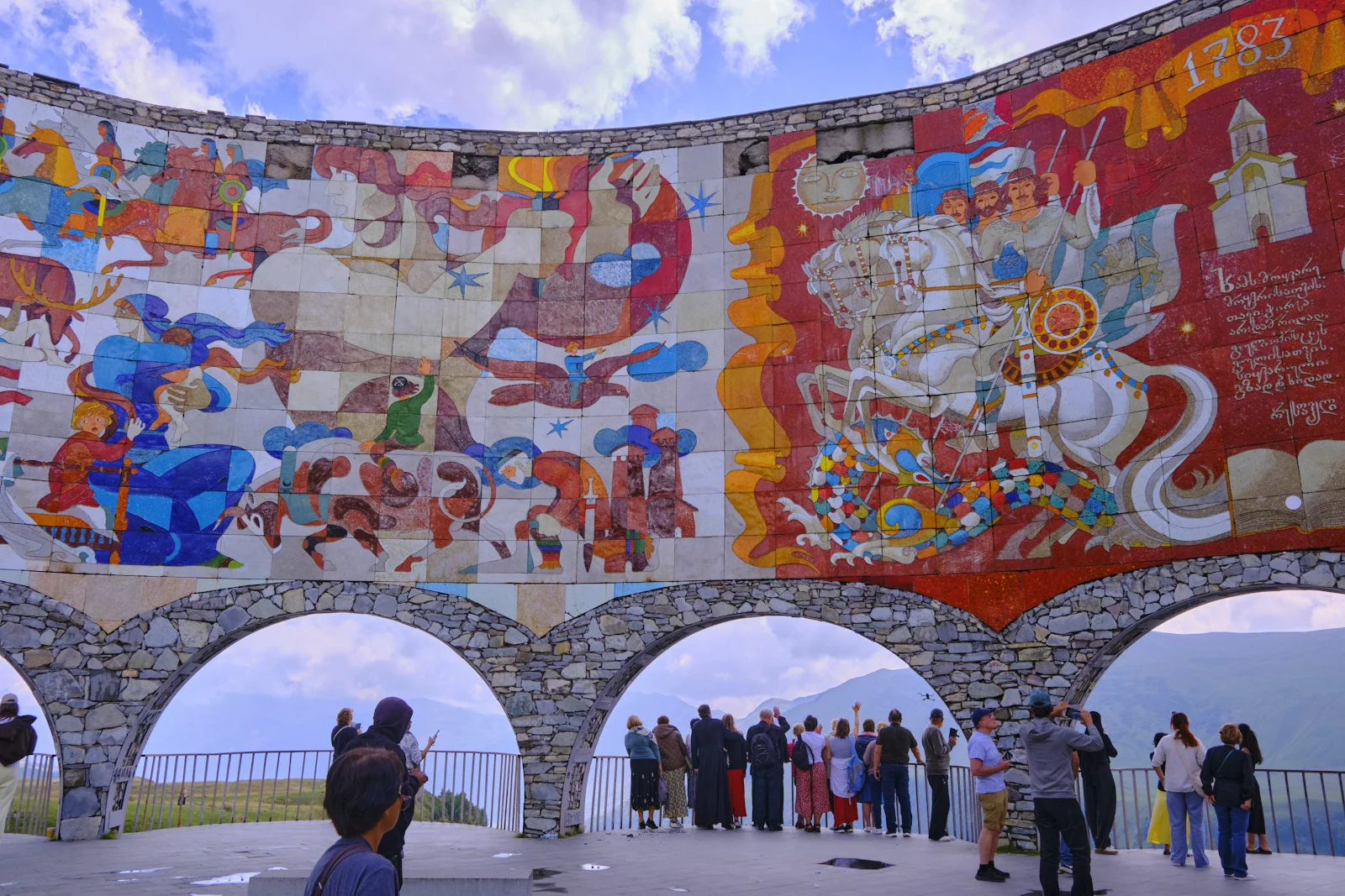 The left half of the Friendship Monument mosaic, St George on a white horse, visitors along the rail.