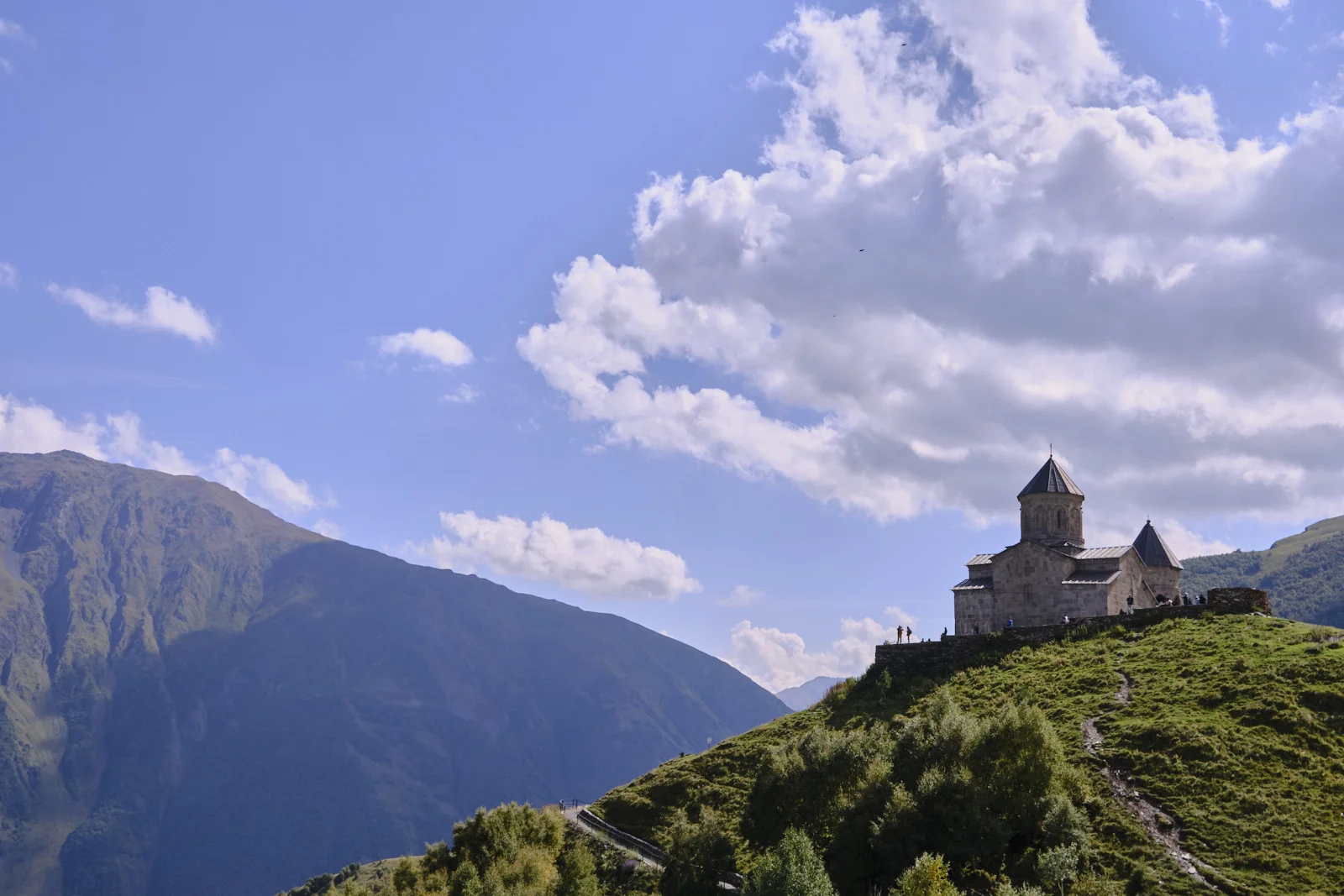 Gergeti Trinity Church on a green hill, a high mountain wall behind it. Gergeti Trinity Church on a green hill, a high mountain wall behind it.