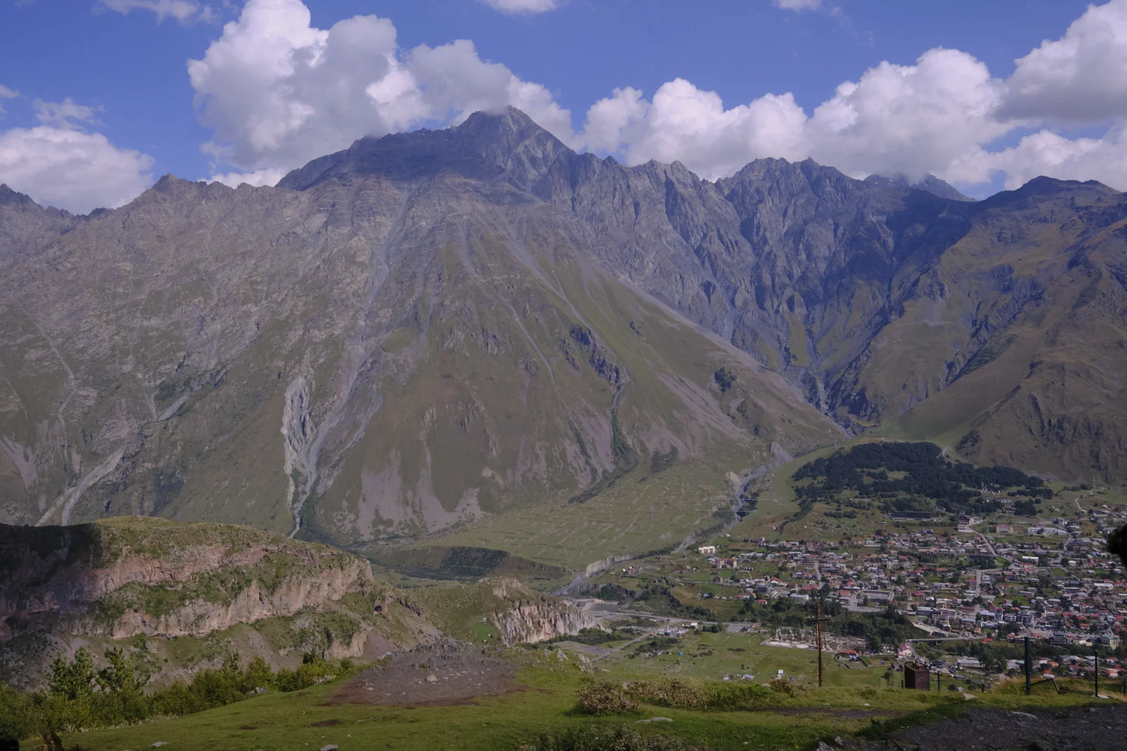 The town of Stepantsminda in a valley under a steep rocky mountain.