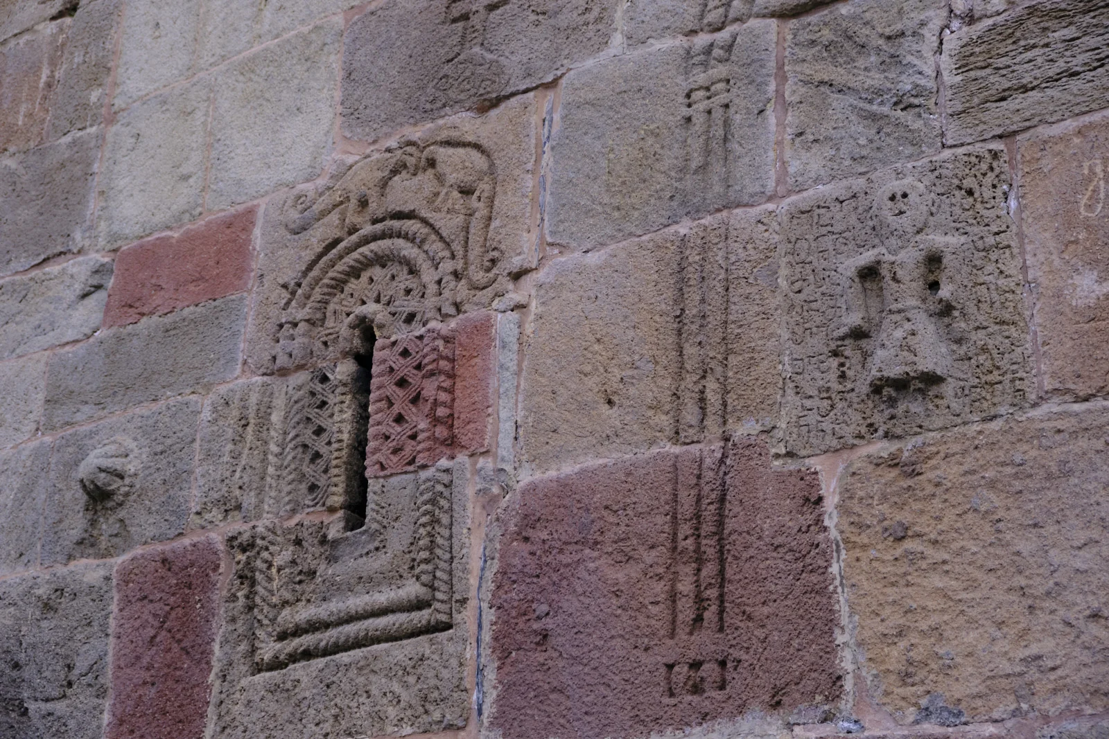A narrow carved window in a wall of red and gray stone, with a small relief figure beside it.