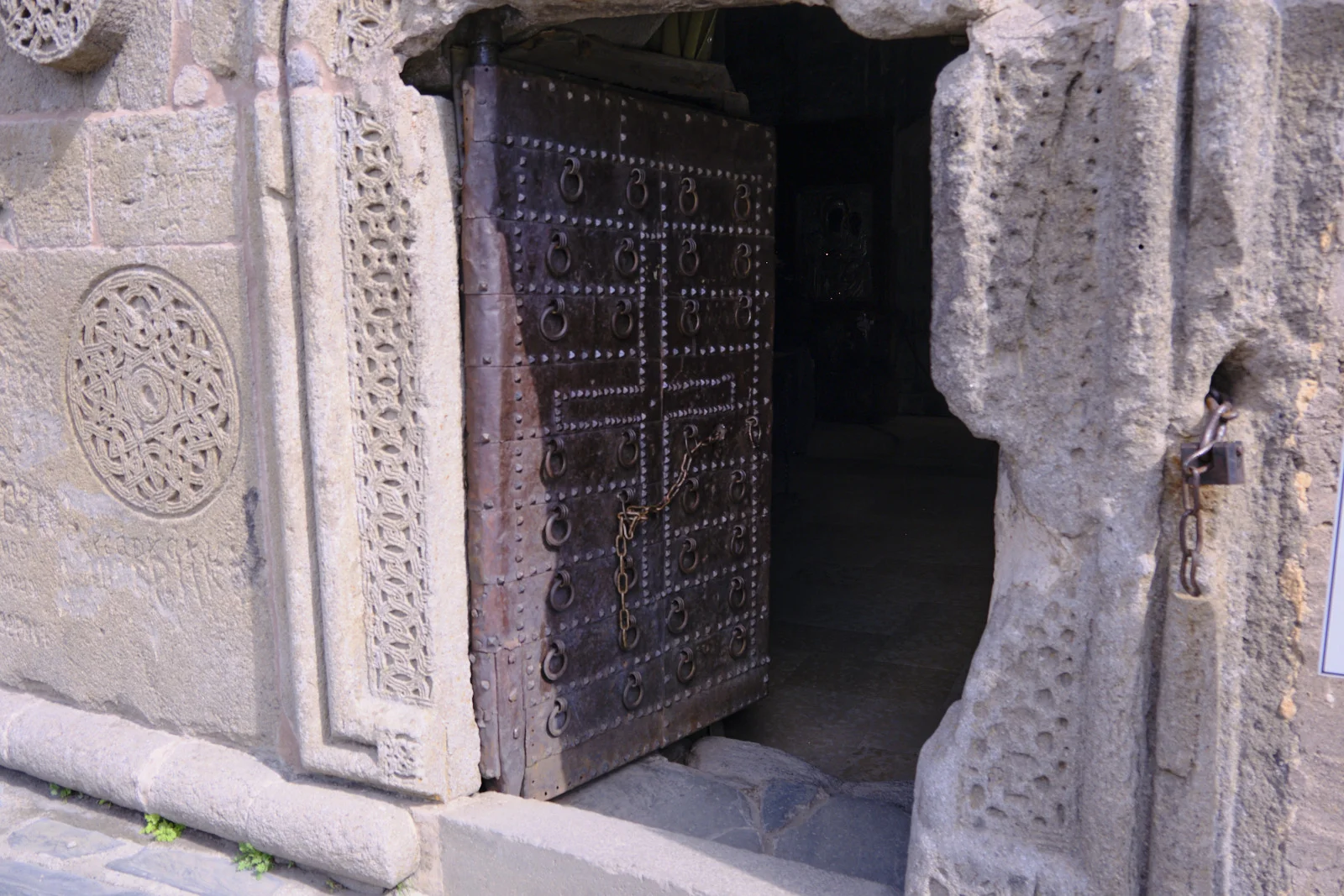 A heavy studded wooden door in a carved stone frame, a round knotwork panel beside it.