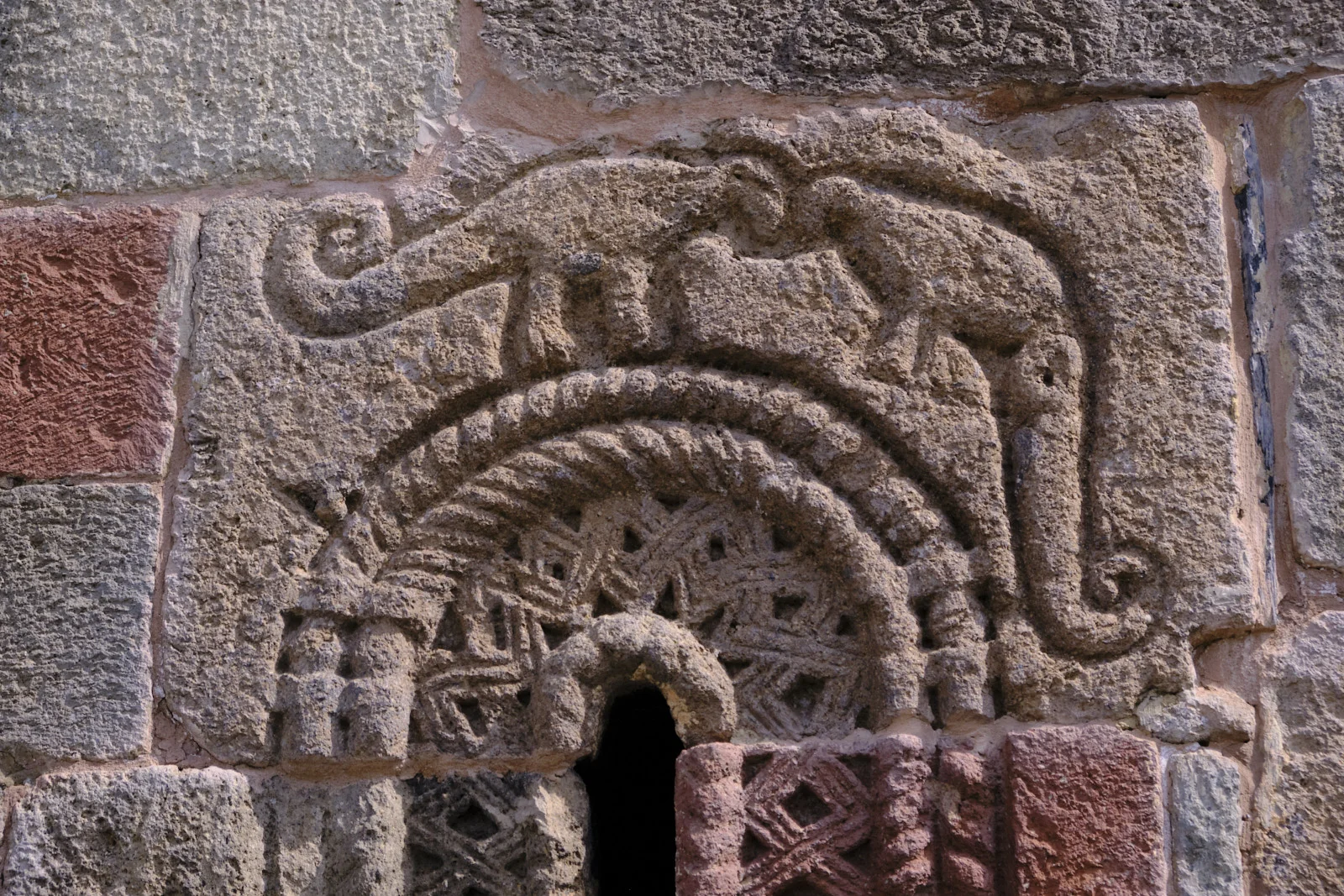 A carved animal, possibly a lion, crouched over a small arched opening.