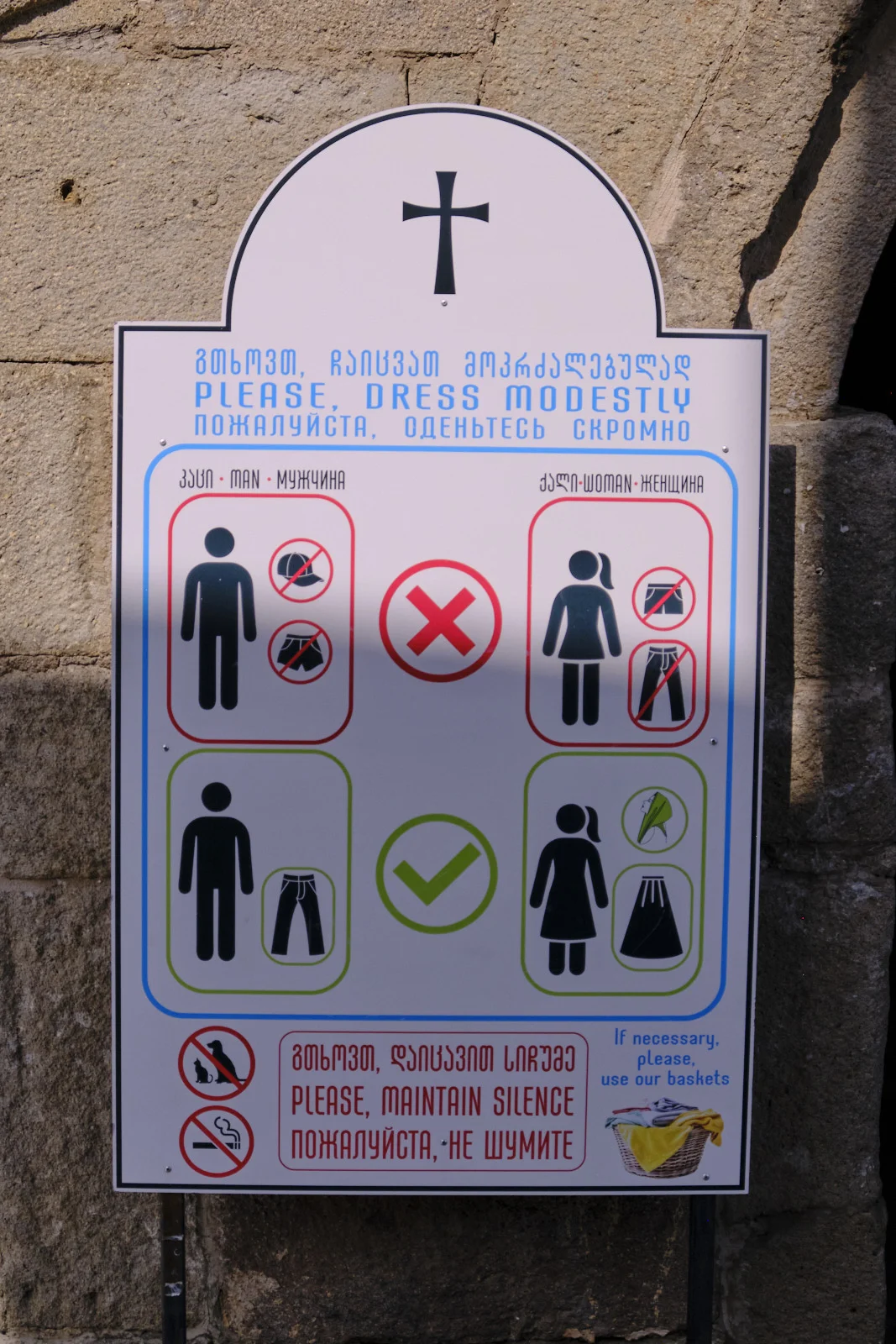 A church sign in Georgian, English, and Russian asking visitors to dress modestly and keep silent.