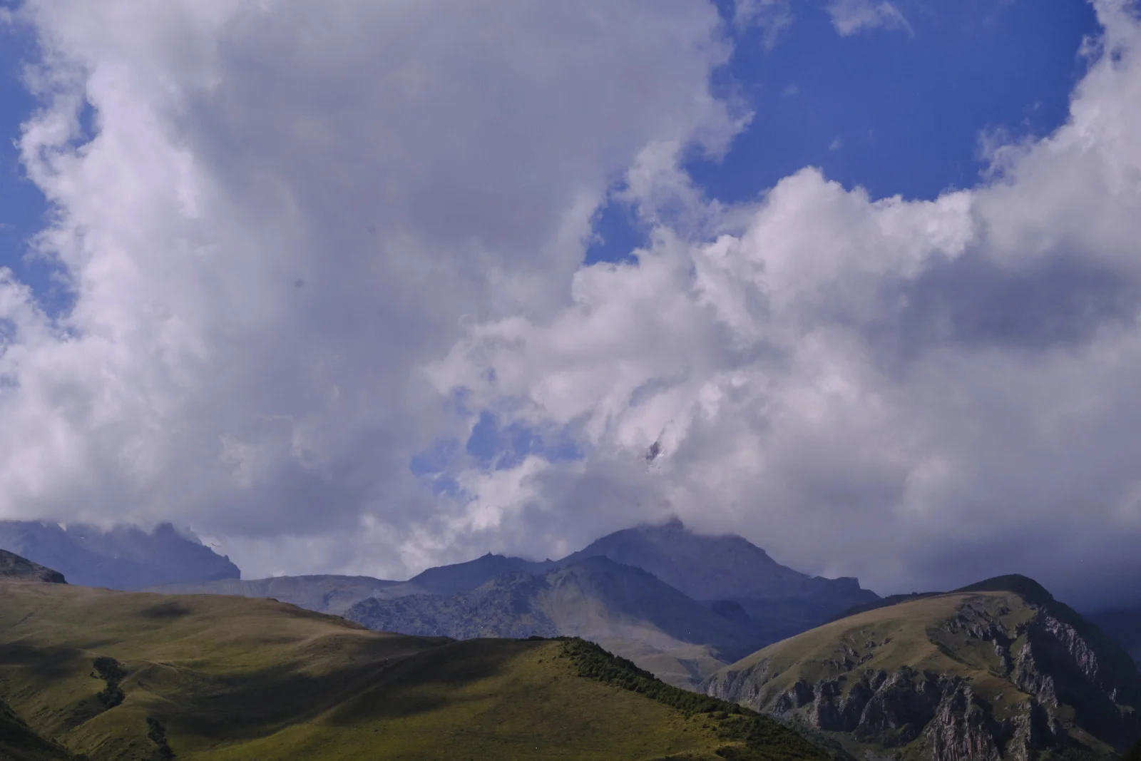 A high peak, Kazbek, half hidden in cloud above dark green ridges.