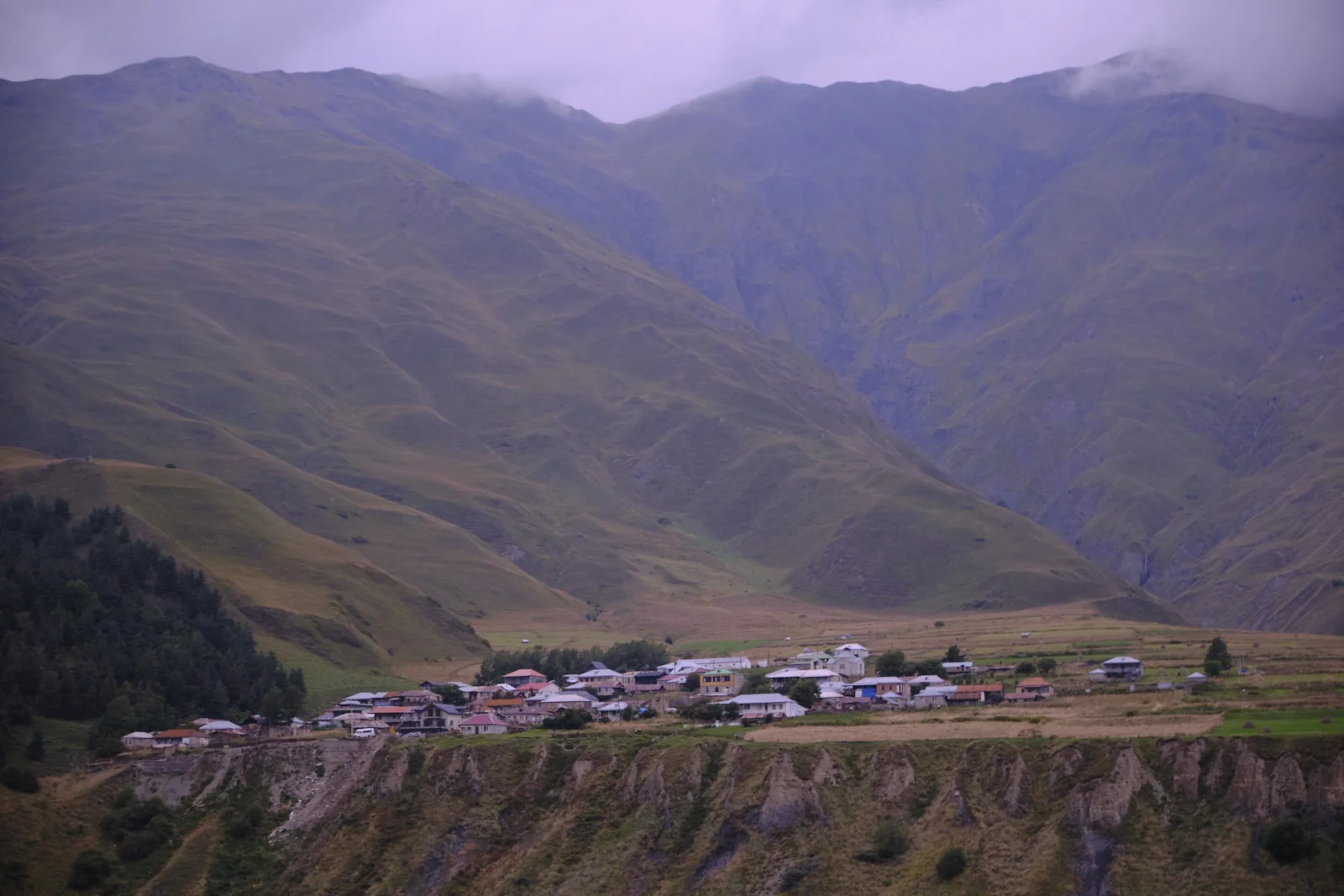 A small village on a shelf of land, folded green mountains behind it.