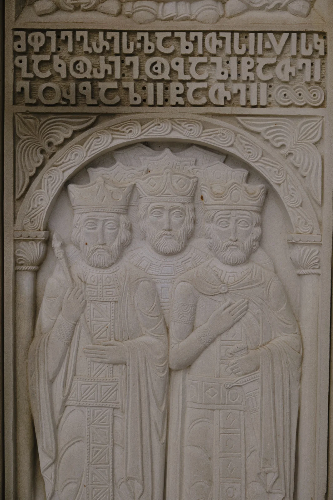 A stone relief of three crowned, bearded figures under an arch of Georgian letters.