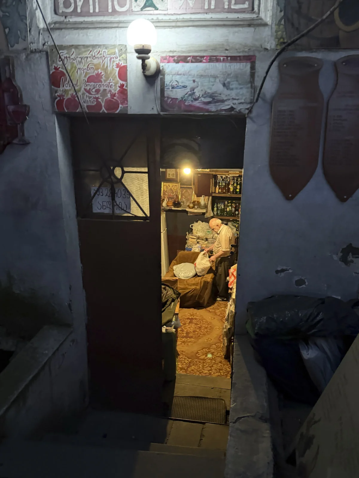 A narrow doorway into a dim wine room, with a man at a counter and wine lists on the wall outside.