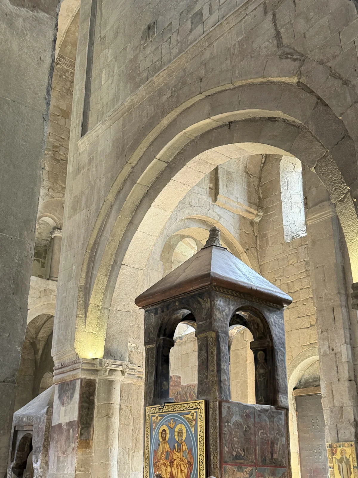 Stone arches inside Svetitskhoveli, with a painted icon screen and a wooden canopy.