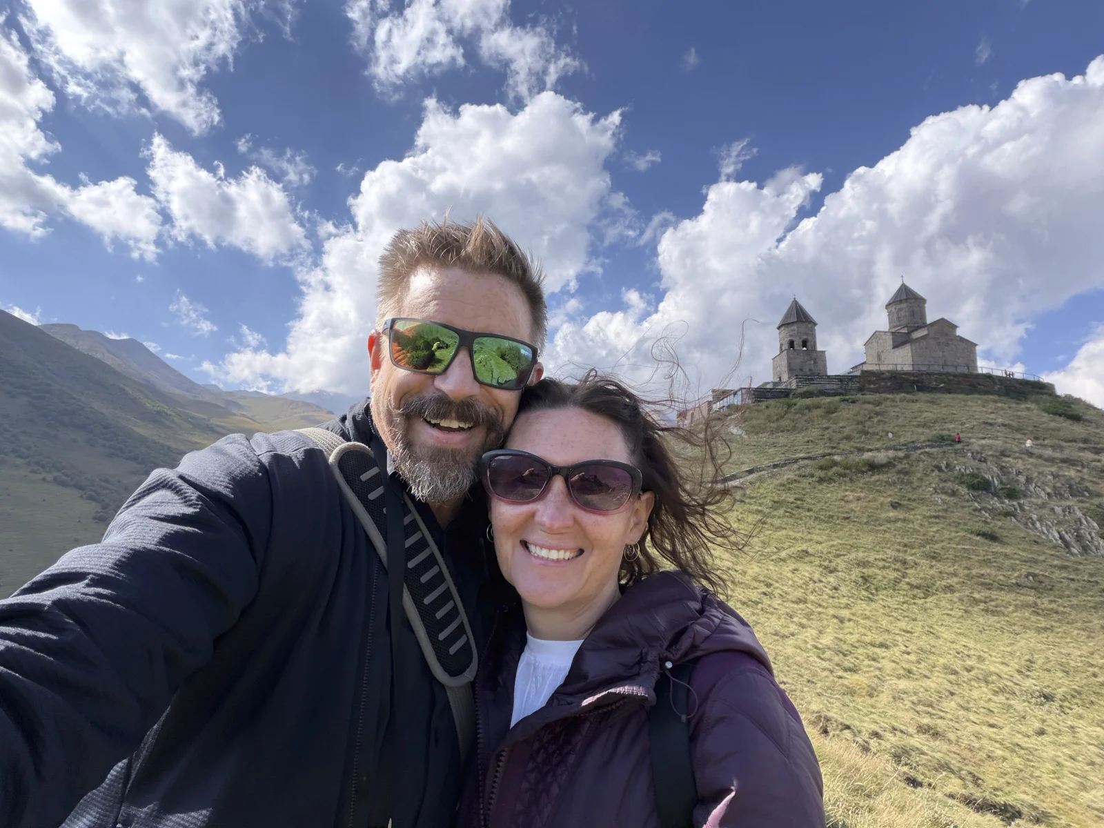 A couple taking a selfie with Gergeti Trinity on the hill behind them.