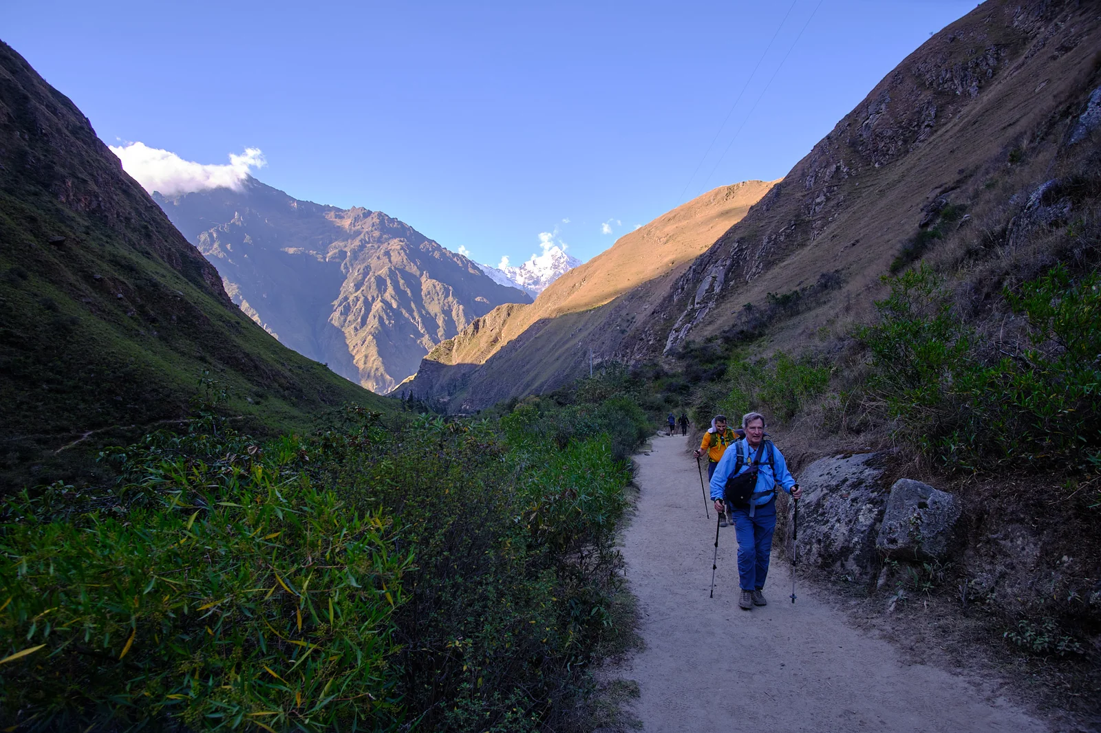 Peter hiking toward the camera on a narrow Inca Trail path through a steep mountain valley in late light