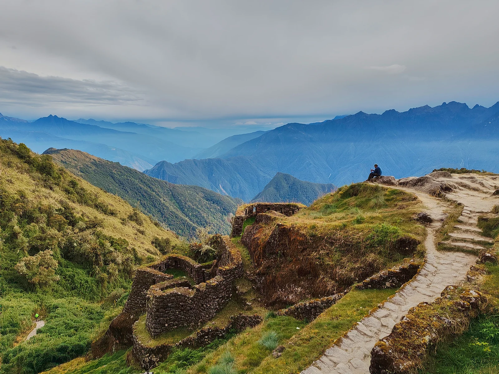 Stone path along the ridge at Phuyupatamarca, with circular Inca walls dropping into cloud-filled valleys