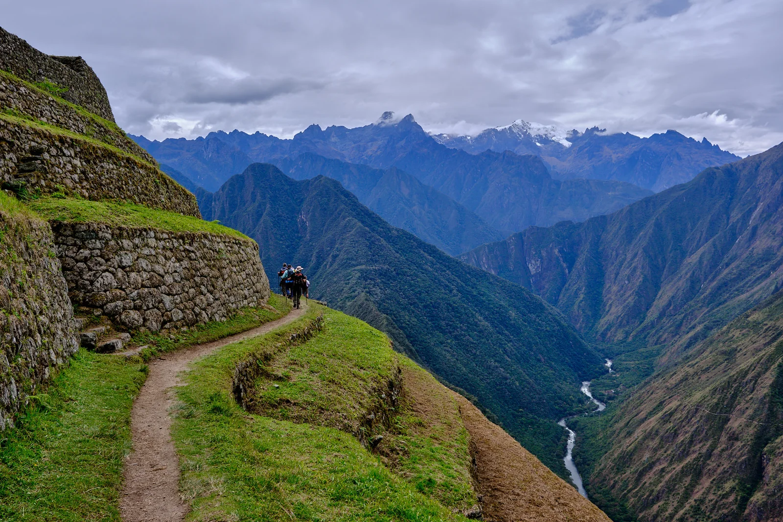 Hikers on a narrow Inca Trail path along stone terraces high above the Urubamba River
