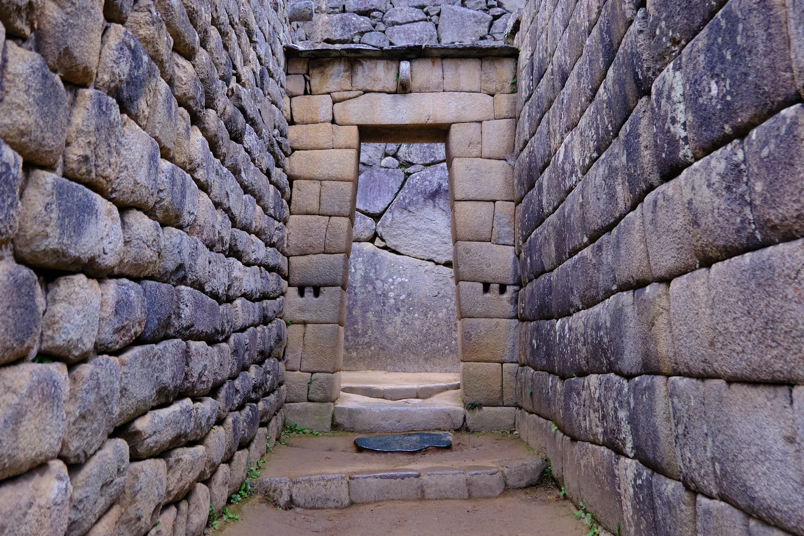 Trapezoidal Inca doorway of fitted stone at Machu Picchu, looking through to a large carved boulder