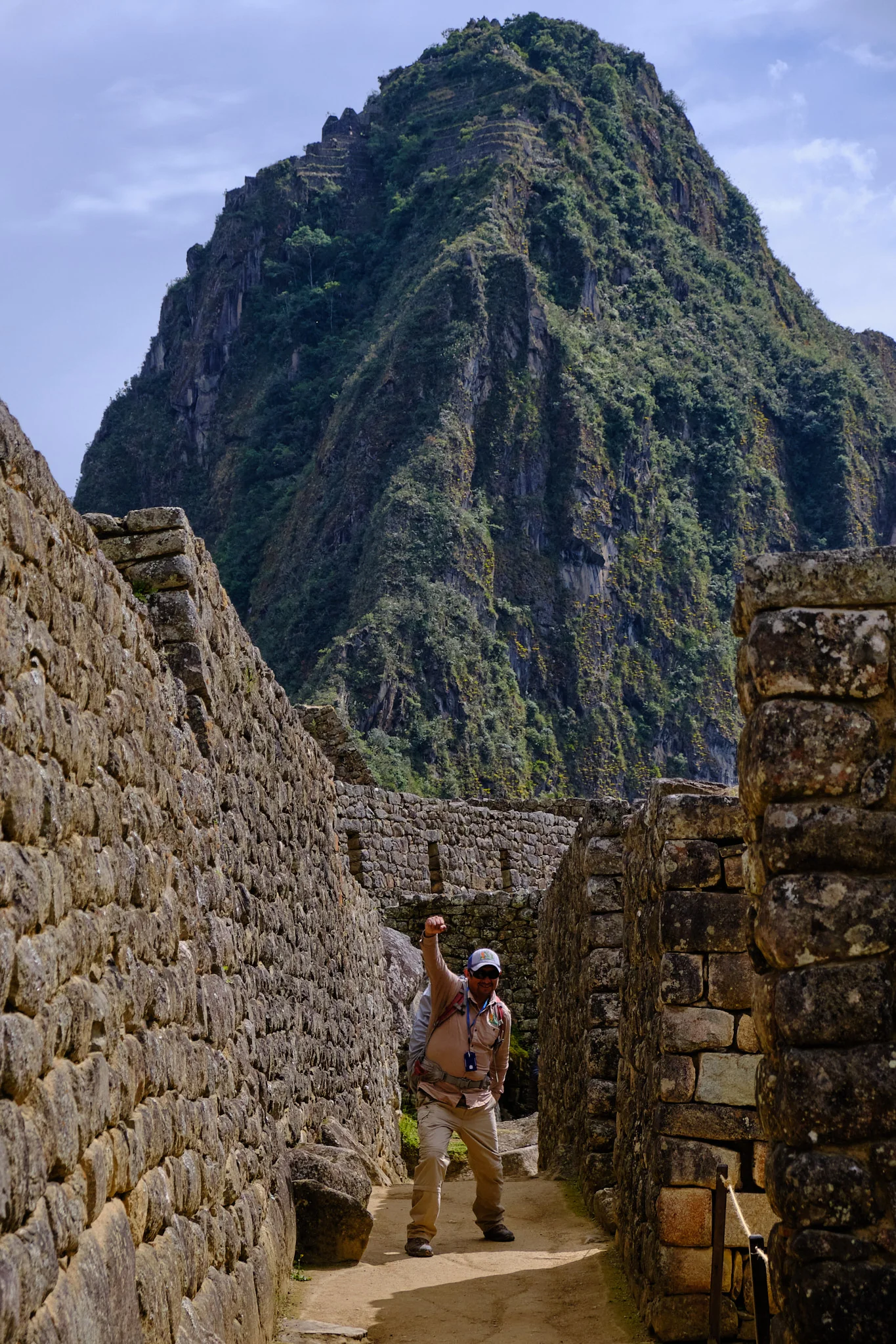 Percy raising a fist in a stone corridor at Machu Picchu, with Huayna Picchu filling the sky behind him