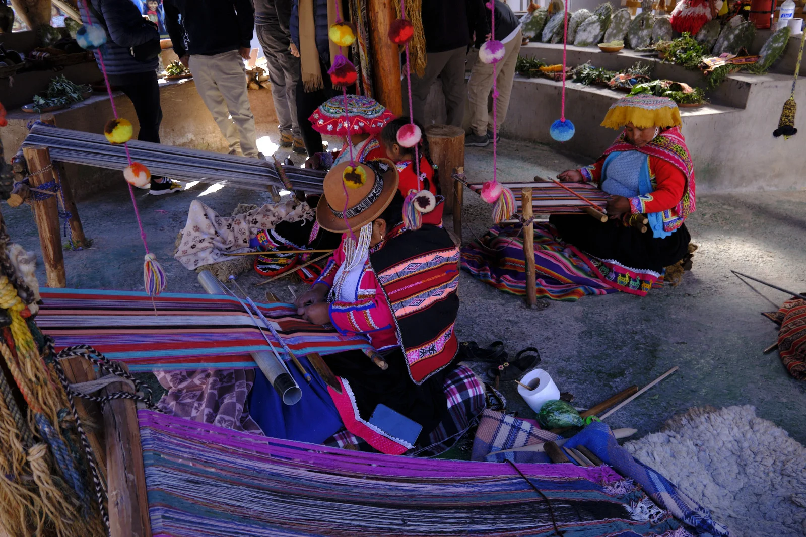 Quechua weavers at backstrap looms, with hanging wool and cactus pads used for cochineal dye, at Ccochahuasi on the Sacred Valley road