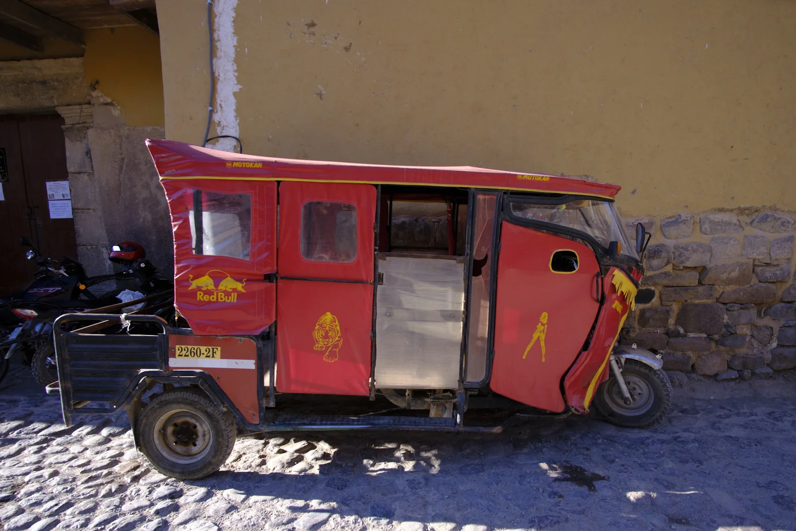 Cobblestone street in Ollantaytambo, with a mototaxi against a yellow wall and Inca stonework