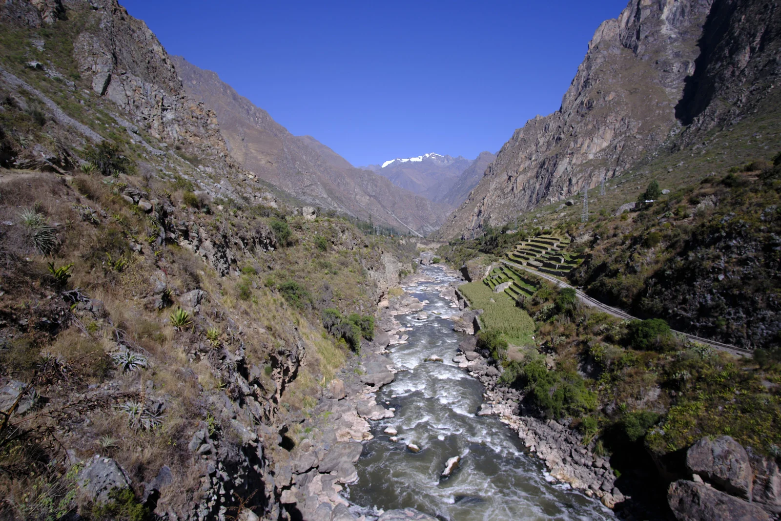 Urubamba River in the canyon below Km 82, with agricultural terraces and the railway on the right bank and Nevado Veronica at the head of the valley