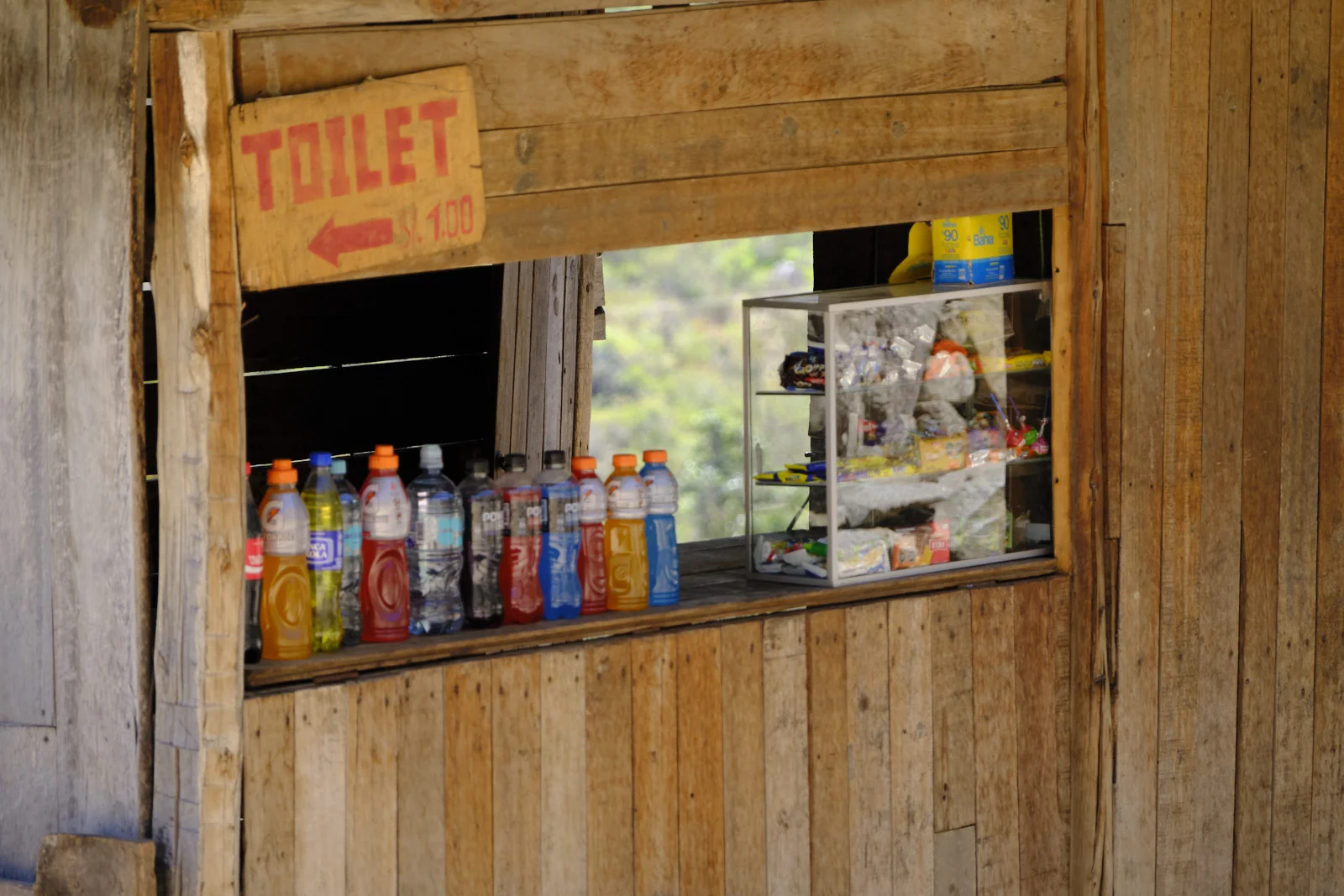 Wooden trail kiosk on day 1, with a painted toilet sign and bottled drinks