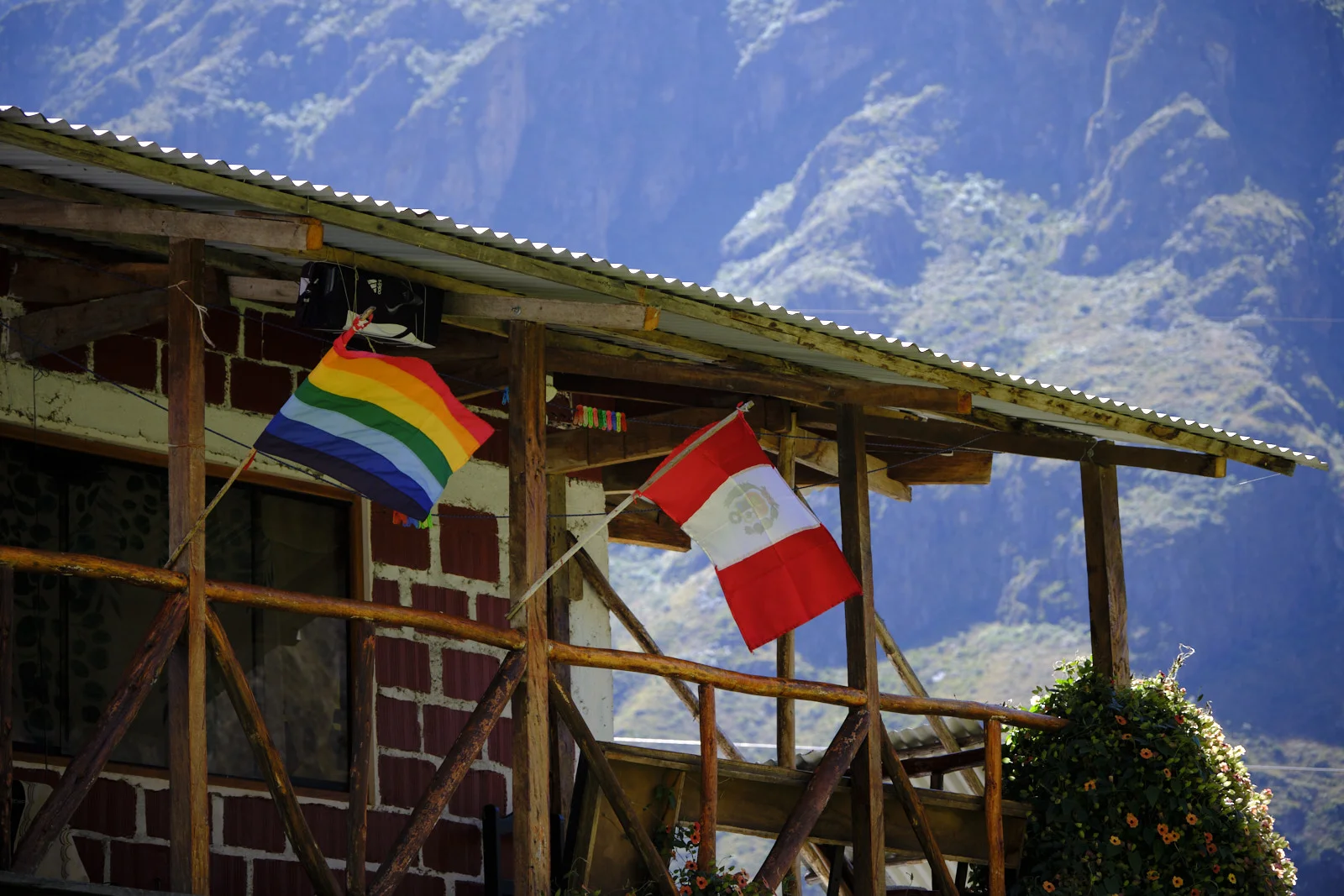 Rainbow flag of Cusco and the Peruvian flag on a brick house with a corrugated roof along the Urubamba valley