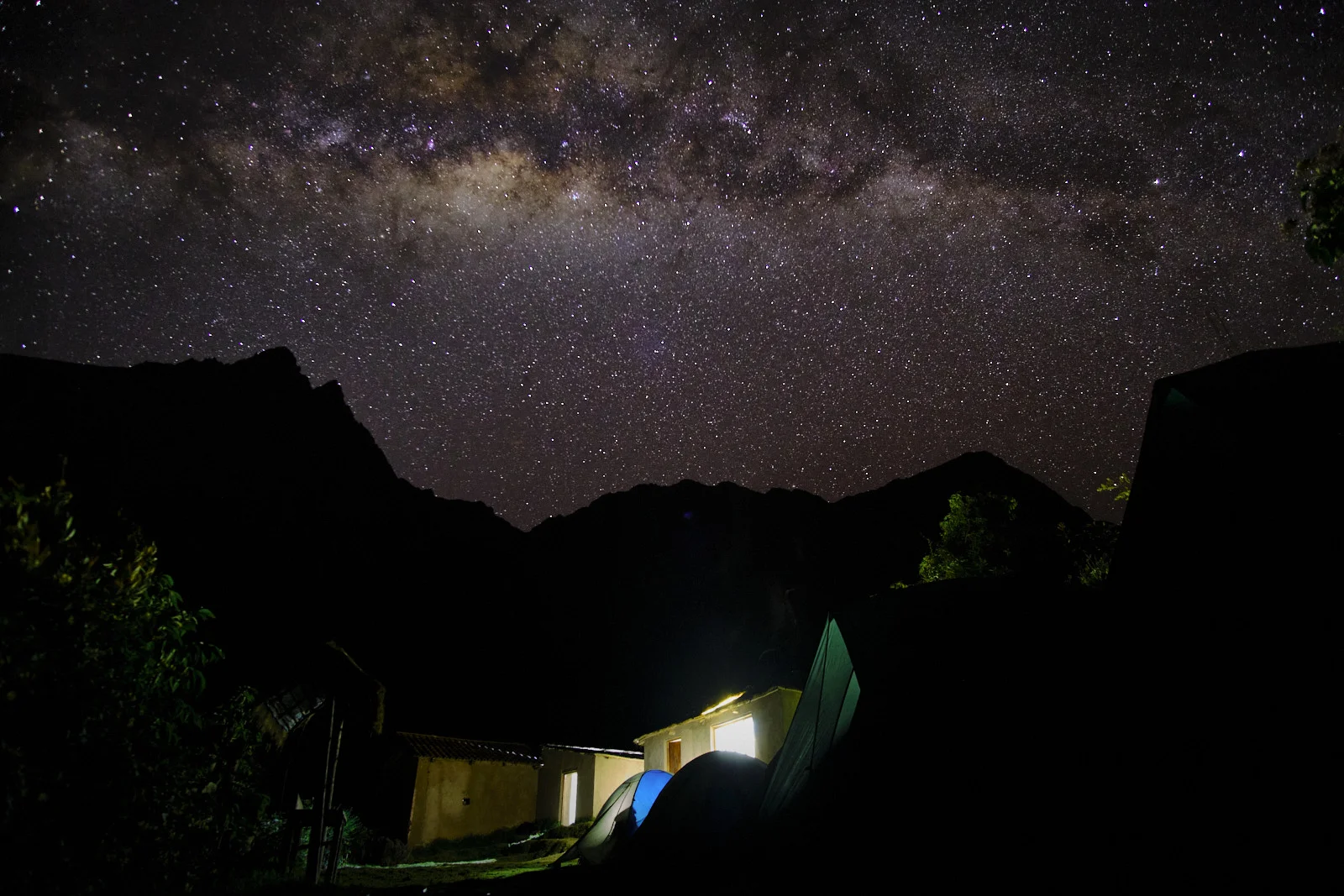 Milky Way over Hatunchaca camp, with lit stone buildings, tents, and silhouetted ridgelines