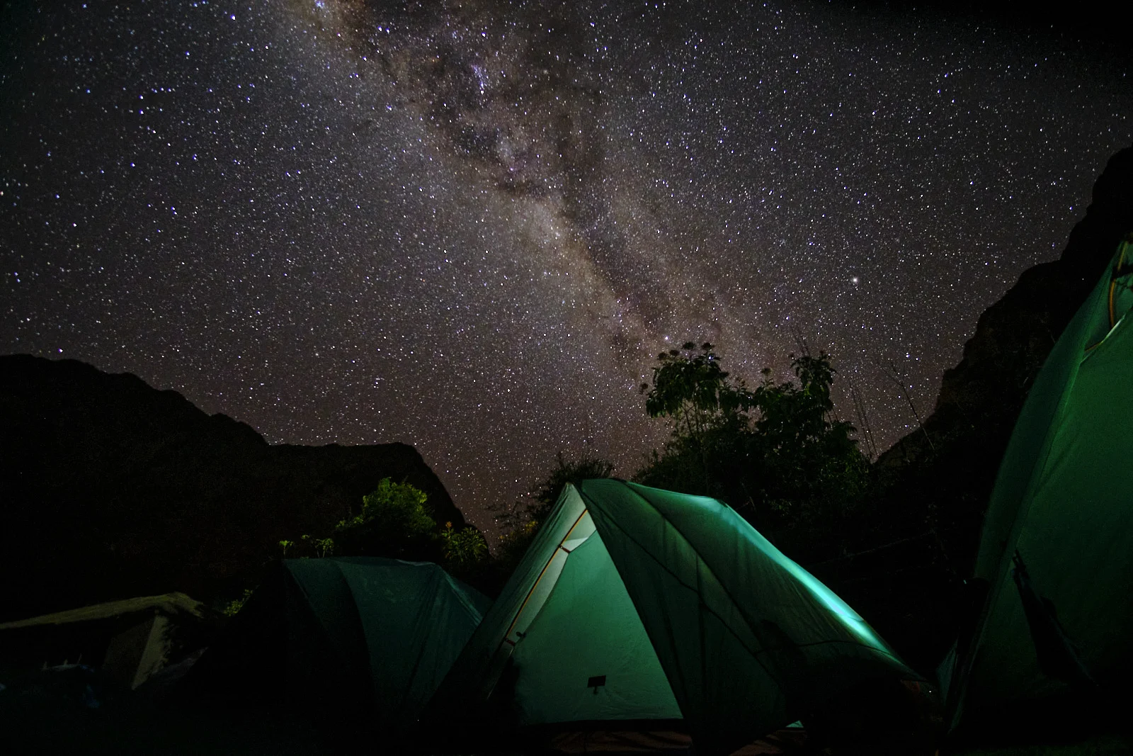 Green tents at Hatunchaca under the Milky Way, with trees and canyon walls in silhouette