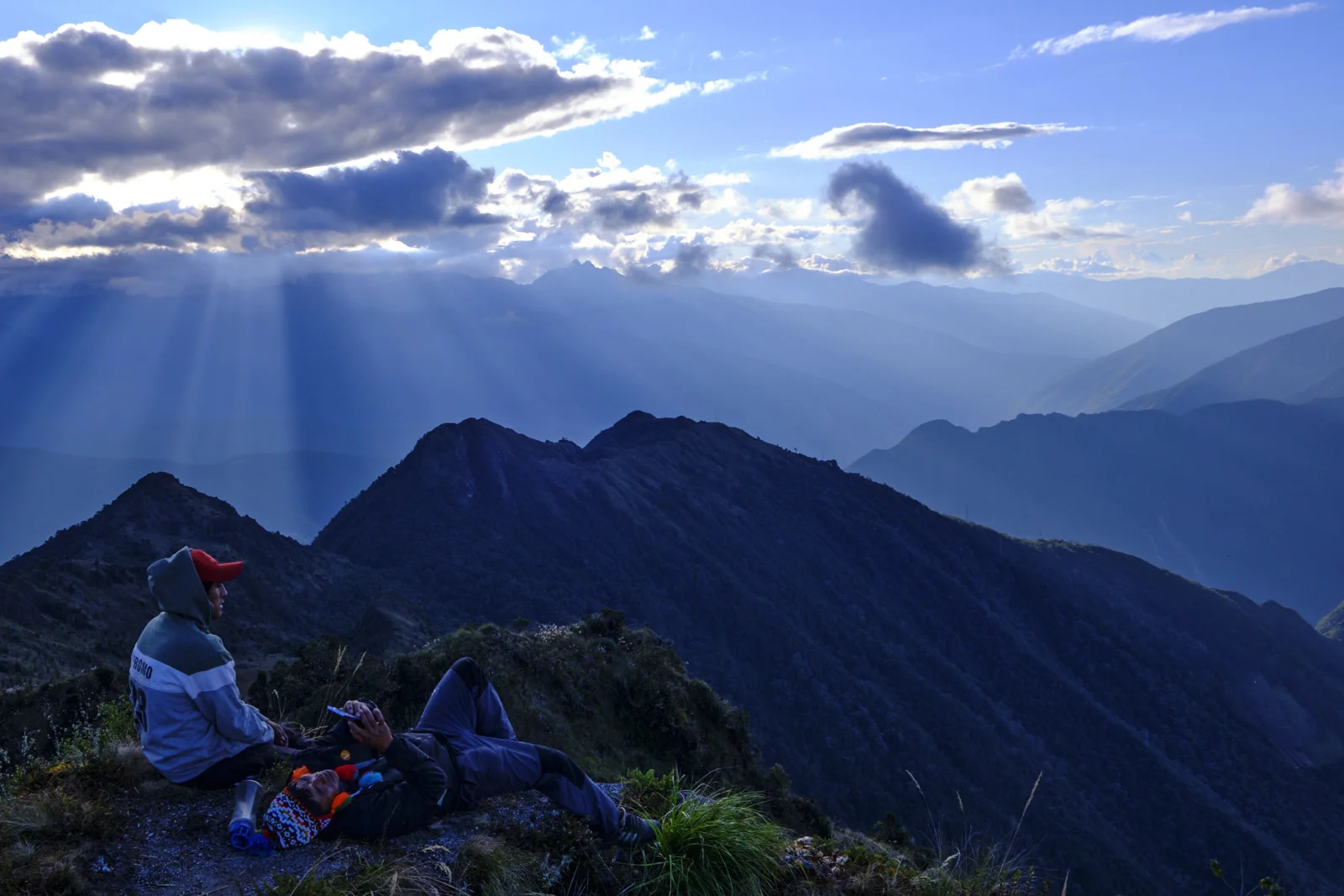 Ridge above Phuyupatamarca camp at sunset, sun rays across the valleys and a dark double-peaked ridge