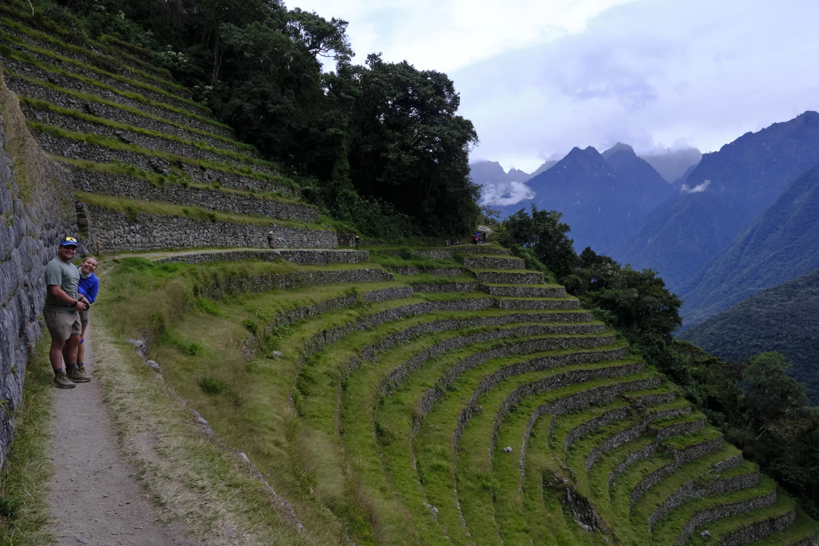 Wiñay Wayna’s curved agricultural terraces on a steep mountainside, a dirt path along the upper wall and the Urubamba valley beyond