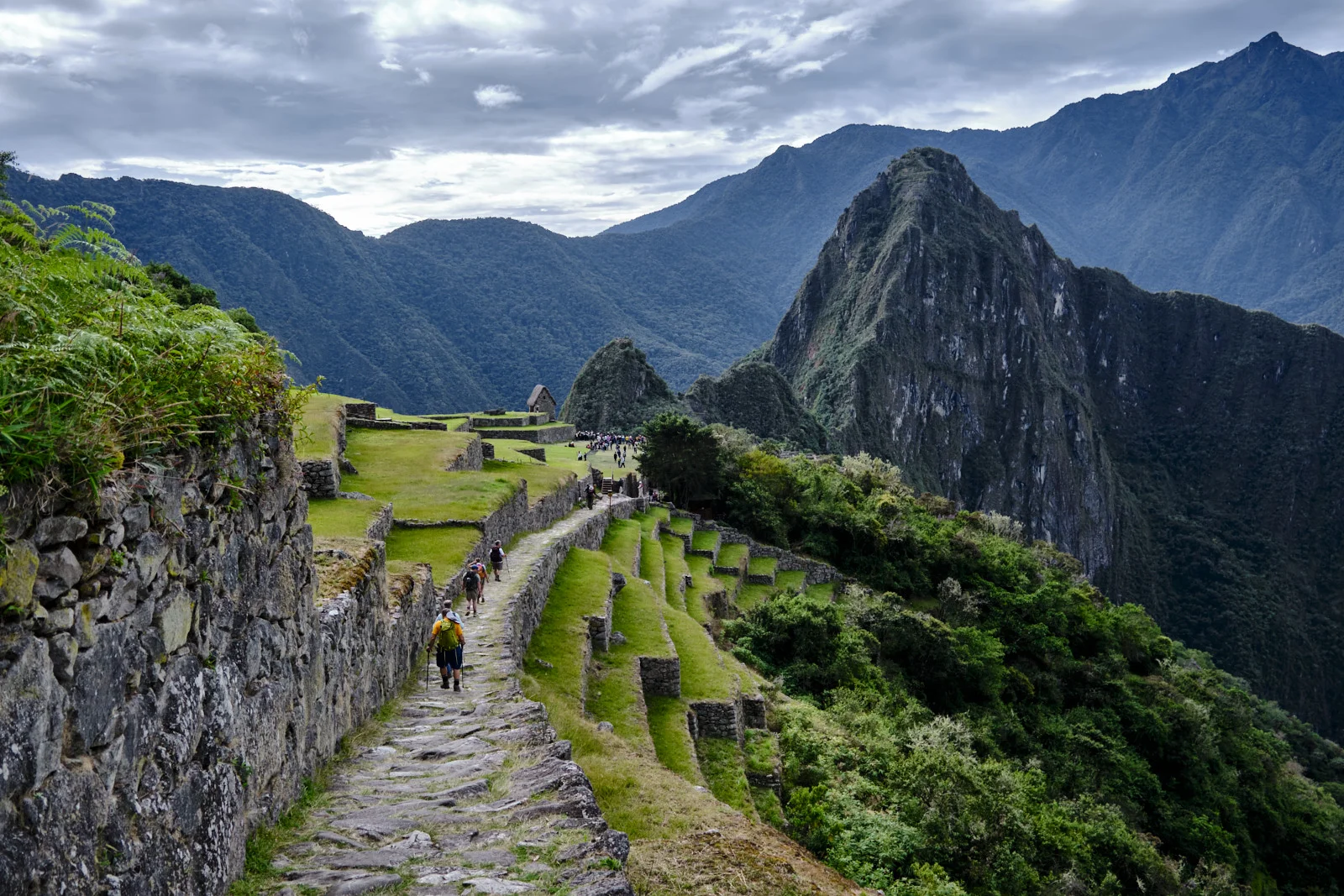 Stone-paved Inca Trail along Machu Picchu’s upper agricultural terraces, toward the citadel with Huayna Picchu and the Guardhouse ahead