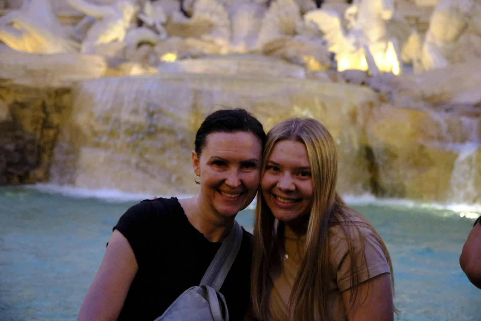 Two people smiling in front of the illuminated Trevi Fountain in Rome