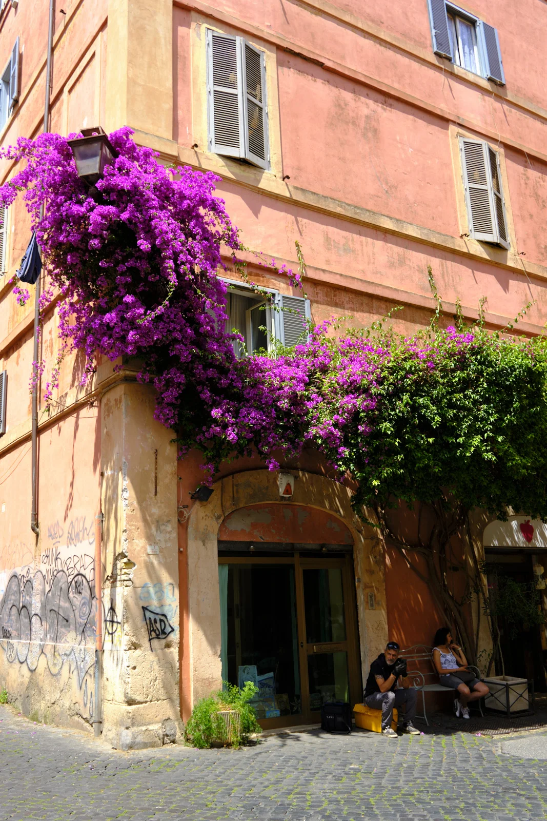 Bougainvillea on a pink Roman apartment building with people sitting in a doorway