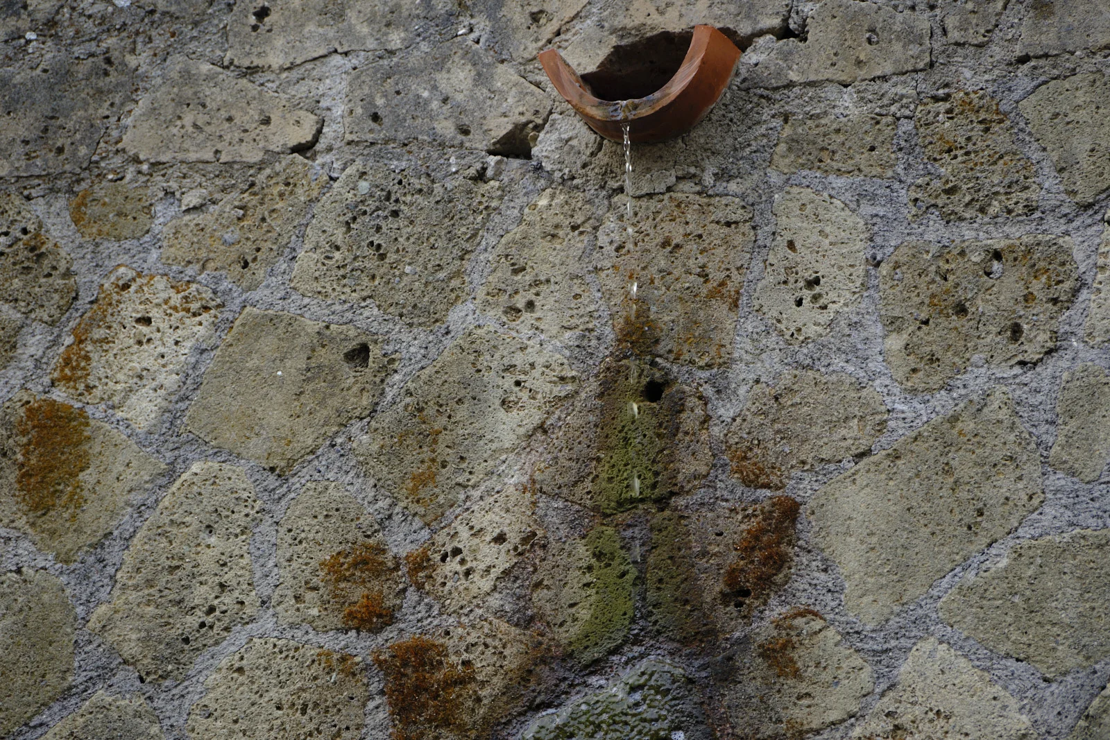 Water dripping from a terracotta pipe in a reticulated stone wall